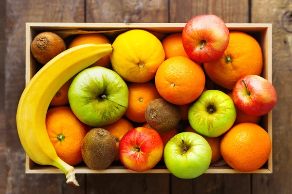 Box full of fresh fruits. Fruit harvest - apples, oranges, lemon, kiwi, banana. Rustic wooden table.