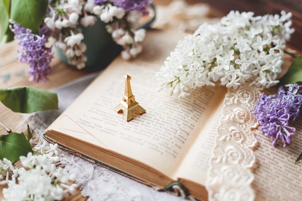 Still life with lilac flowers, book, lace bookmark and miniature Eiffel tower.