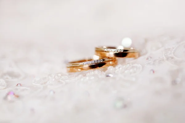 Golden wedding ringswith diamonds lie on lace silk fabric. Symbol of love and marriage.Wedding embroidery dress detail.