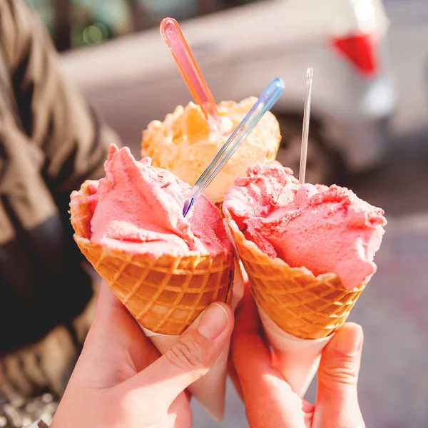 Three colorful tasty ice-cream cones in hands. Sunny background with cold desserts in hands of friends.