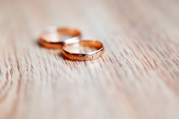 Golden wedding rings with ornament on wooden background.
