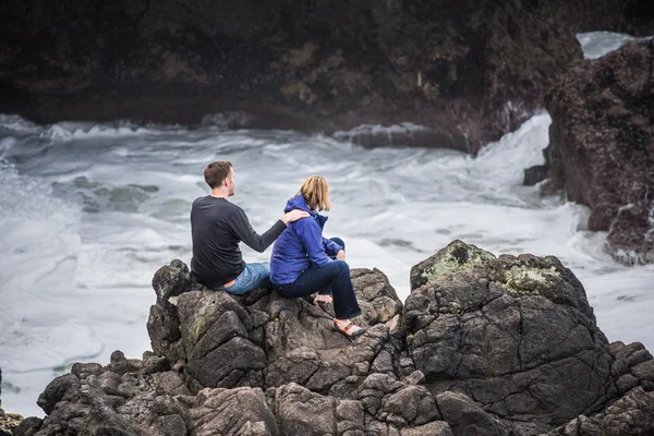 Two hikers couple giving massage on ocean cliff in cold Cape Perpetua Oregon