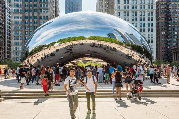 Chicago bean in Millennium Park with many people and buildings in background and two young guys taking a picture