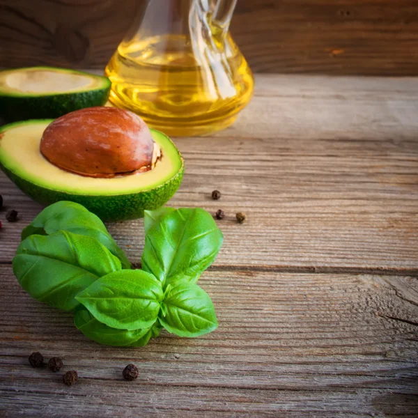 Food background with avocado, basil and olive oil on old wooden
