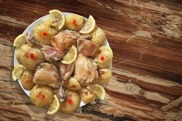 Plate of Fried Chicken Legs with Potato and Lemon Slices on Old Wooden Table