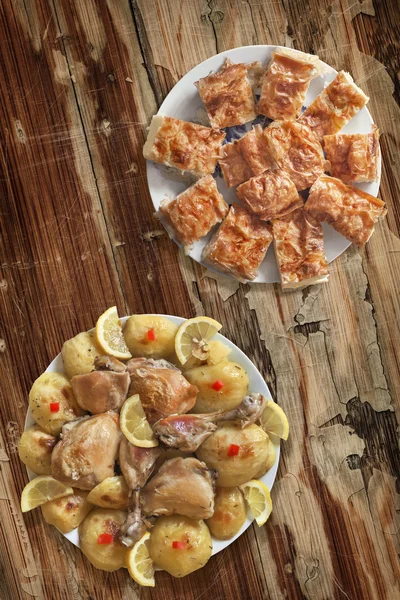 Plates of Fried Lemon Chicken Legs with Potato and Serbian Gibanica Cheese Pie on Old Wooden Table