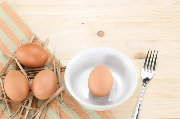 Fresh eggs on thatch and one egg in bowl with fork ,on wood background.