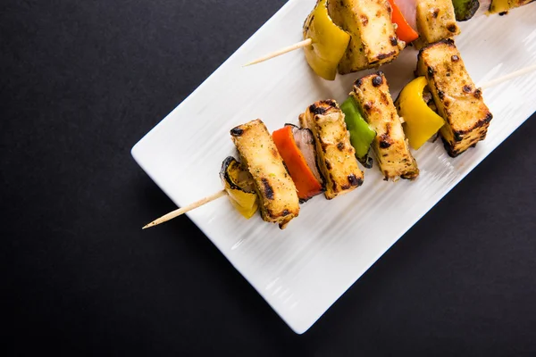 Paneer Tikka Kabab - Tandoori Indian cheese skewers, malai paneer tikka / malai paneer kabab, chilli paneer served in white plate with barbecue stick and green sauce, selective focus