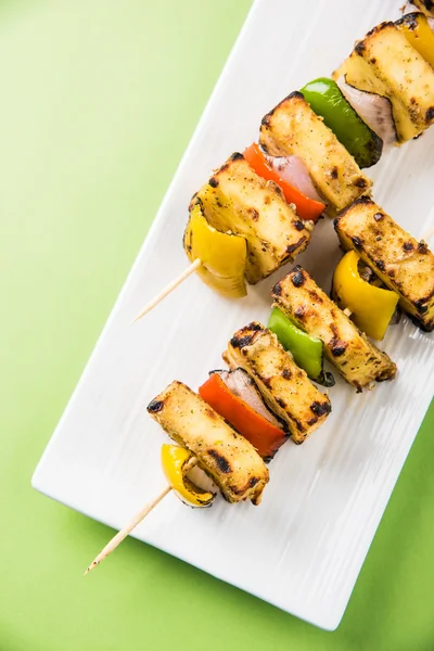 Paneer Tikka Kabab - Tandoori Indian cheese skewers, malai paneer tikka / malai paneer kabab, chilli paneer served in white plate with barbecue stick and green sauce, selective focus