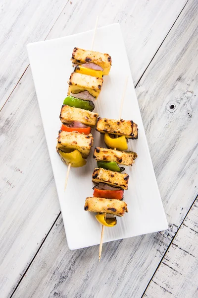 Paneer Tikka Kabab - Tandoori Indian cheese skewers, malai paneer tikka / malai paneer kabab, chilli paneer served in white plate with barbecue stick and green sauce, selective focus