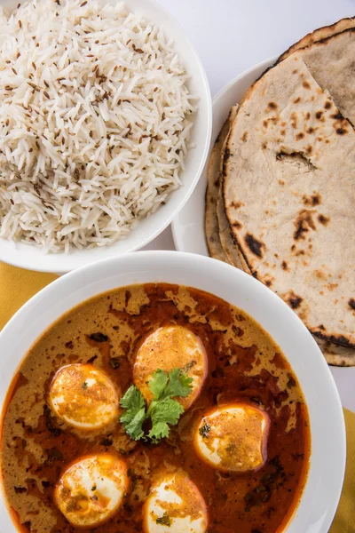 Egg curry with roti/chapati and jeera rice, tasty and spicy anda curry with roti and rice, indian egg masala curry served in ceramic bowl with roti, salad and jeera rice
