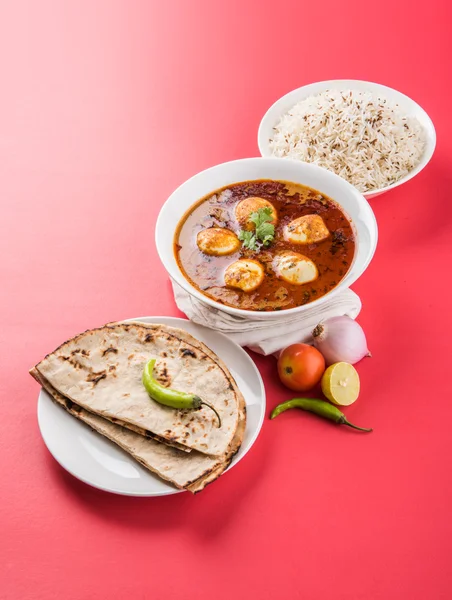 Egg curry or anda curry with roti/chapati and jeera rice, tasty and spicy anda curry with roti and rice, indian egg masala curry served in ceramic bowl with roti, salad and jeera rice
