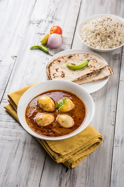 Egg curry with roti/chapati and jeera rice, tasty and spicy anda curry with roti and rice, indian egg masala curry served in ceramic bowl with roti, salad and jeera rice
