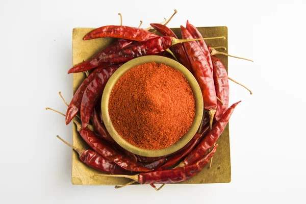 Closeup of red dry chilli powder with red dry chillies in a round brass bowl and square brass plate,front view, isolated on white background, indian spices
