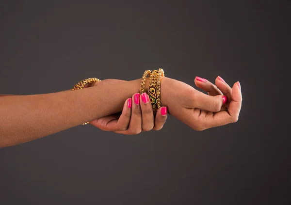 Gold bangles in hand, graceful poses of girls hand wearing gold bangles, designer gold bangles and hand, girls hands with golden bangles, closeup, isolated on gray background