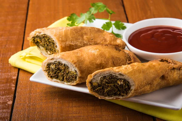 Spring rolls or kothimbir vadi or sambar vadi or coriander spring rolls, indian snacks, tastes great with tea and tomato ketchup or tomato sauce, in square white plate over colourful background