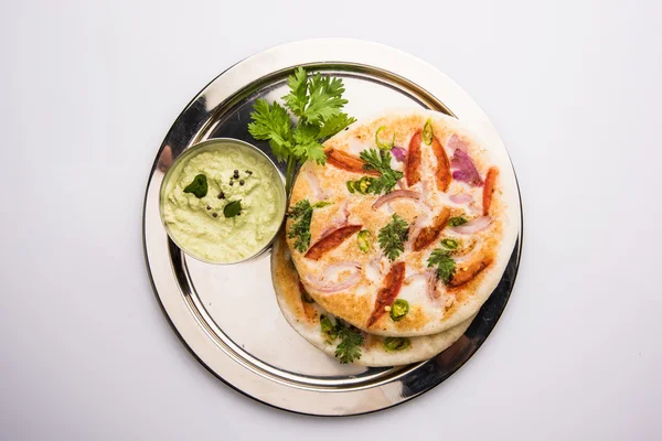 South indian food, two uttapam with coconut chutney in white ceramic plate with coriander leaf, closeup and front view, isolated on white background