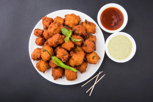 Delicious Tasty and Yummy Indian Moong Dal vada or moong dal pakoda or moong vada or moong vade or Pakora (Fritter) with fried green chilli, red and green hot sauce.