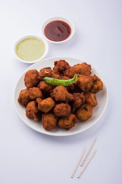 Delicious Tasty and Yummy Indian Moong Dal vada or moong dal pakoda or moong vada or moong vade or Pakora (Fritter) with fried green chilli, red and green hot sauce.
