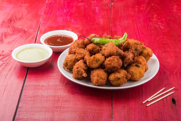 Delicious Tasty and Yummy Indian Moong Dal vada or moong dal pakoda or moong vada or moong vade or Pakora or pakode (Fritter) with fried green chilli, red and green hot sauce.