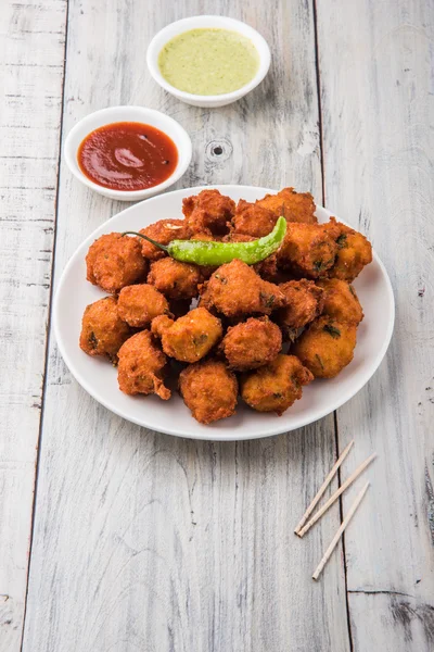 Delicious Tasty and Yummy Indian Moong Dal vada or moong dal pakoda or moong vada or moong vade or Pakora or pakode (Fritter) with fried green chilli, red and green hot sauce.