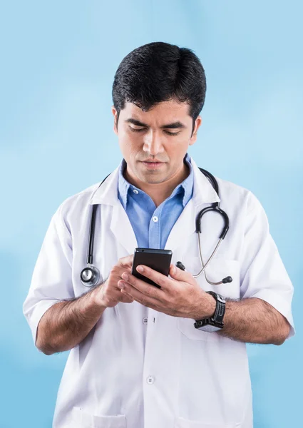 Portrait of confident indian male doctor showing smart phone over blue background. indian doctor with smart phone, asian doctor pointing smart phone