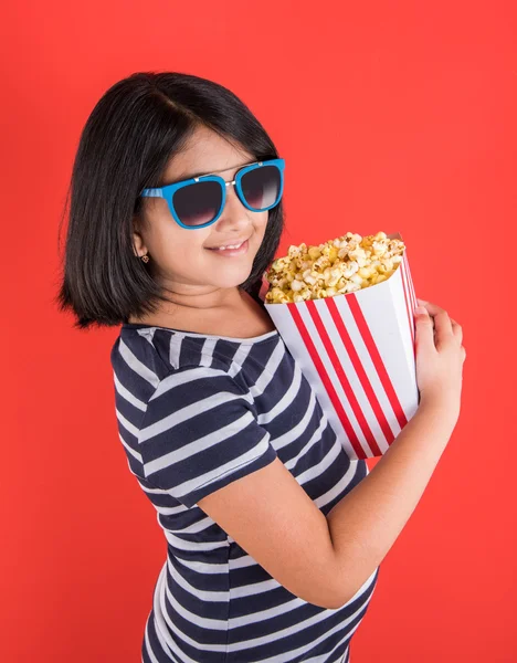 Happy girl eating popcorn and wearing glasses, indian girl eating popcorn, asian girl and popcorn, small girl eating popcorn on red background