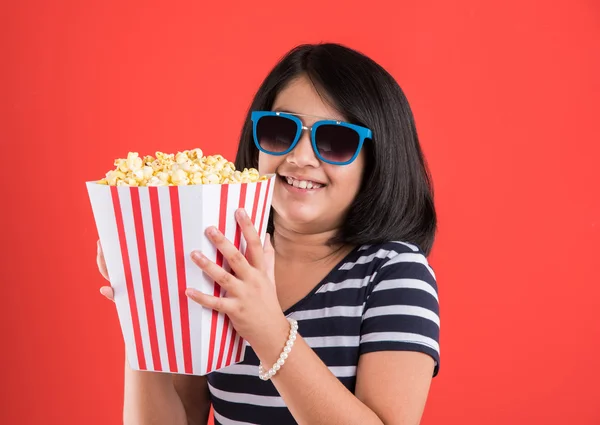 Happy girl eating popcorn and wearing glasses, indian girl eating popcorn, asian girl and popcorn, small girl eating popcorn on red background