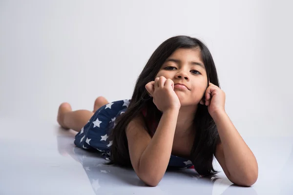Indian cute girl lying on the floor resting her head in her hands, asian Little girl laughing, lying on her stomach, isolated over white background