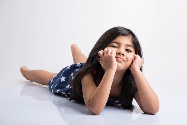 Indian cute girl lying on the floor resting her head in her hands, asian Little girl laughing, lying on her stomach, isolated over white background