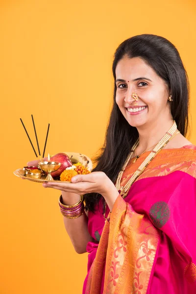 Indian woman performing puja, indian girl with pooja thali or puja thali, portrait of a beautiful young lady with pooja thali, isolated over yellow background