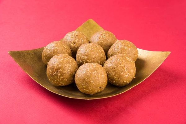 The indian sesame sweet or tilgul laddu, made up of jaggery and sesame seeds, indian sweet for Makar Sankranti festival, in terracotta bowl with jaggery & raw sesame