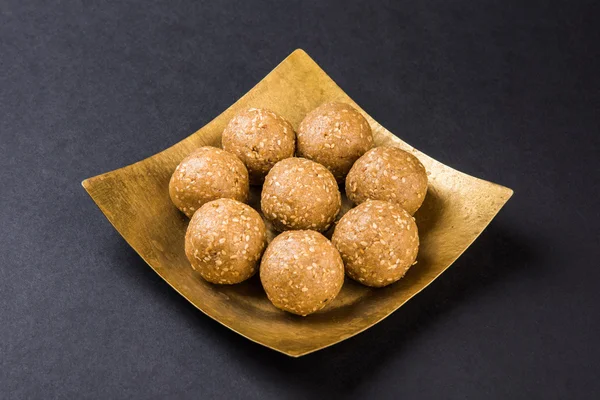 The indian sesame sweet or tilgul laddu, made up of jaggery and sesame seeds, indian sweet for Makar Sankranti festival, in terracotta bowl with jaggery & raw sesame