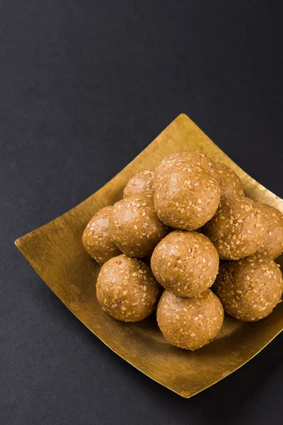 The indian sesame sweet or tilgul laddu, made up of jaggery and sesame seeds, indian sweet for Makar Sankranti festival, in terracotta bowl with jaggery & raw sesame