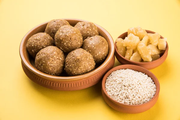 The indian sesame sweet or tilgul laddu, made up of jaggery and sesame seeds, indian sweet for Makar Sankranti festival, in terracotta bowl with jaggery & raw sesame