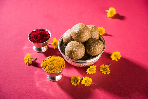 Sesame laddu or tulgul or til gul laddu or ladu in brass plate with huldi and kumkum, indian traditional festival in january, indian sweet food, indian rituals, tilgul cake or vadi