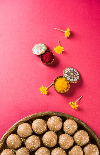 Sesame laddu or tulgul or til gul laddu or ladu in brass plate with huldi and kumkum, indian traditional festival in january, indian sweet food, indian rituals, tilgul cake or vadi