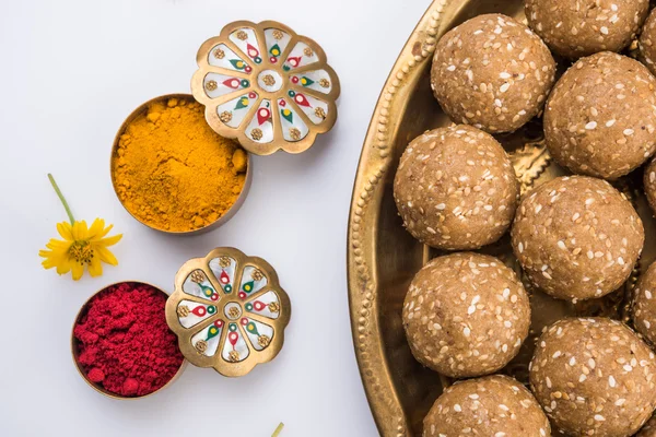 Sesame laddu or tulgul or til gul laddu or ladu in brass plate with huldi and kumkum, indian traditional festival in january, indian sweet food, indian rituals, tilgul cake or vadi