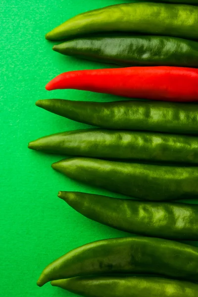 Dipicting uniqueness concept, different concept, special concept, originality concept, against stream concept using fresh red and green chillies, chillies on green background, isolated