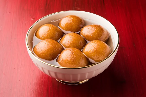 Gulab Jamun served in a square brass plate with pouring sweet syrup - An Indian sweet dish, round shaped, black or brown texture served as a dessert, high calories, diwali food