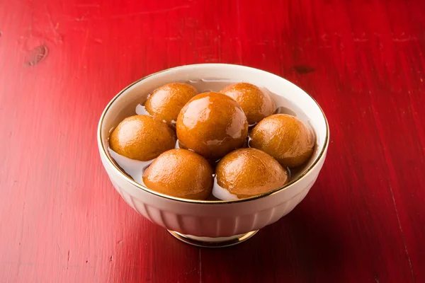 Gulab Jamun served in a square brass plate with pouring sweet syrup - An Indian sweet dish, round shaped, black or brown texture served as a dessert, high calories, diwali food