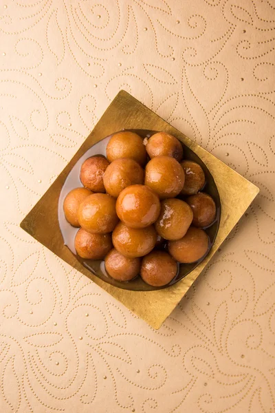 Gulab Jamun served in a square brass plate with pouring sweet syrup - An Indian sweet dish, round shaped, black or brown texture served as a dessert, high calories, diwali food