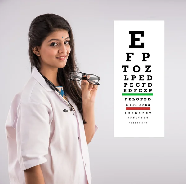 An Indian female nurse with a specs or spectacle or eye wear and eye test chart in the background, isolated on gray background