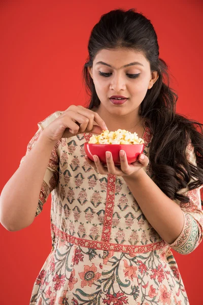 Indian young and beautiful girl eating popcorn, asian girl enjoying popcorn or pop corn, isolated on red background