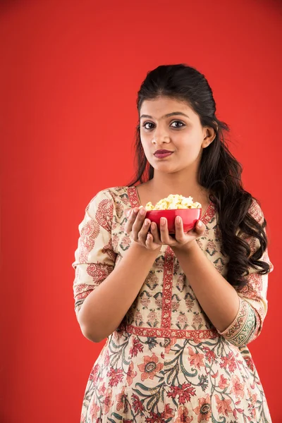 Indian young and beautiful girl eating popcorn, asian girl enjoying popcorn or pop corn, isolated on red background