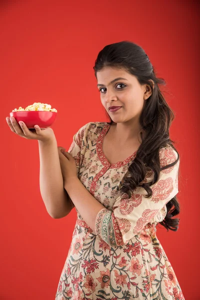 Indian young and beautiful girl eating popcorn, asian girl enjoying popcorn or pop corn, isolated on red background