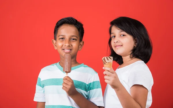 Two happy indian kids and ice cream, two asian kids enjoying ice cream or cone or chocolate candy, girl and boy eating ice cream, isolated on red background,