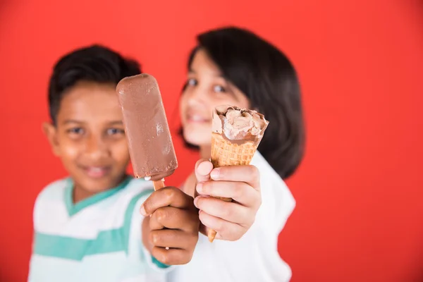 Two happy indian kids and ice cream, two asian kids enjoying ice cream or cone or chocolate candy, girl and boy eating ice cream, isolated on red background,