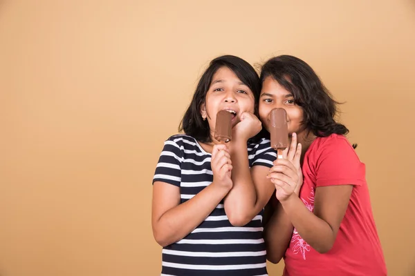 Two indian girls eating ice cream or ice candy, two asian girl and ice cream or ice candy, isolated on brown background, ten year old indian girls enjoying ice cream or ice candy or choko bar