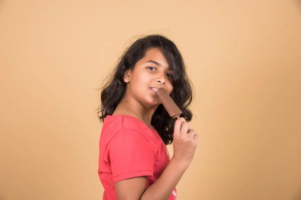 Indian girl eating ice cream or ice candy, asian girl and ice cream or ice candy, isolated on brown background, ten year old indian girl enjoying ice cream